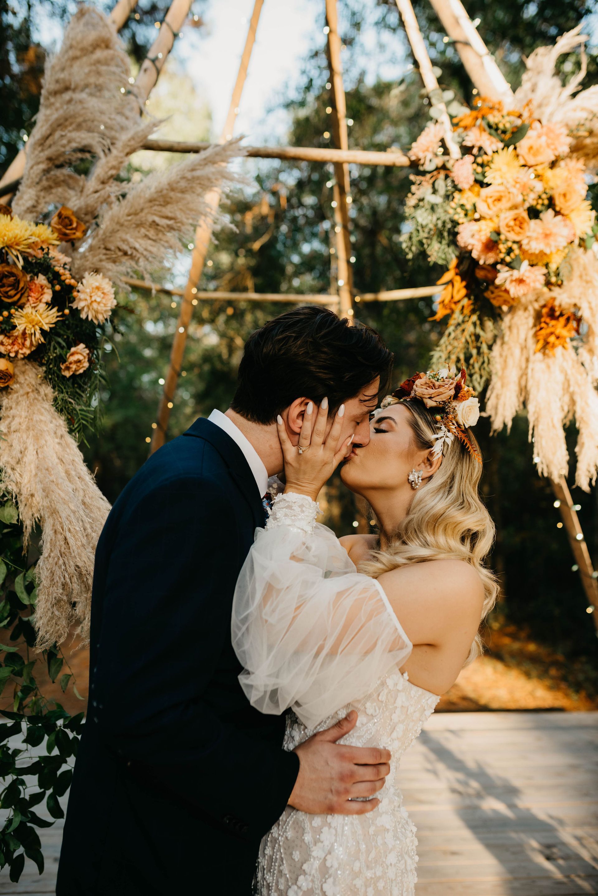 a bride and groom are kissing under a floral arch at their wedding .