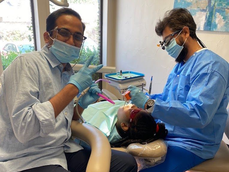 Two dentists are examining a young girl 's teeth in a dental office.