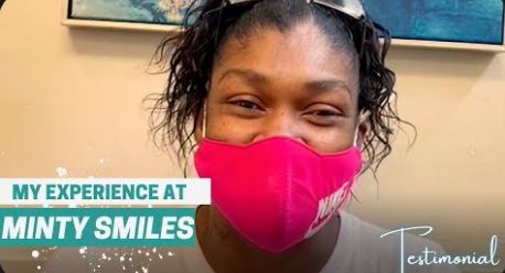 A woman wearing a pink face mask is smiling.