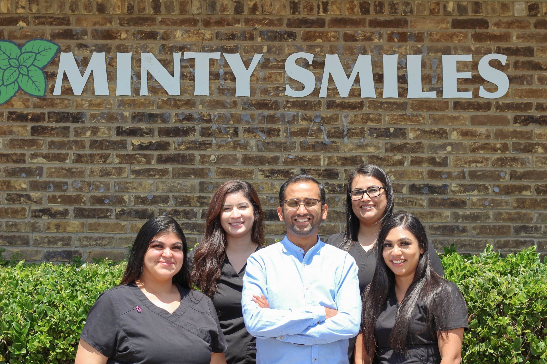 A group of people are posing for a picture in front of a minty smiles sign.