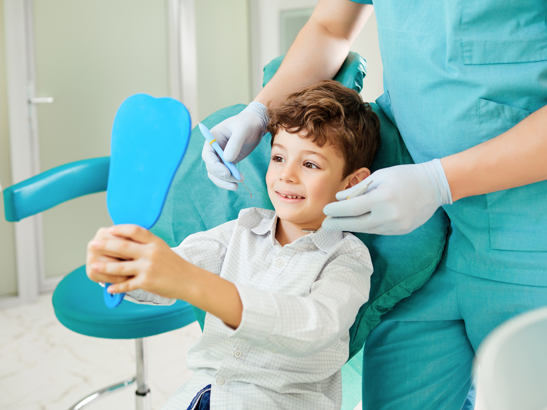 a young boy is sitting in a dental chair looking at his teeth in a mirror .