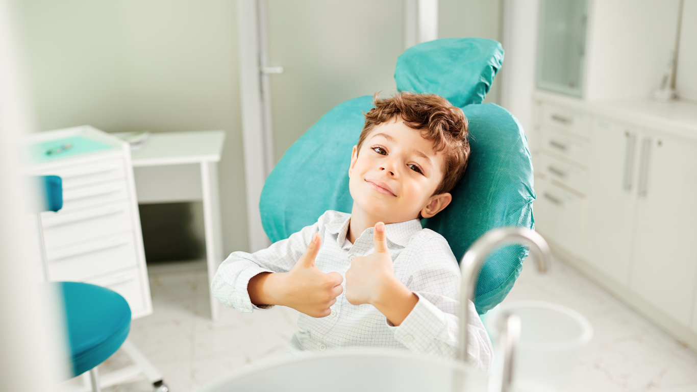 a young boy is sitting in a dental chair giving a thumbs up .