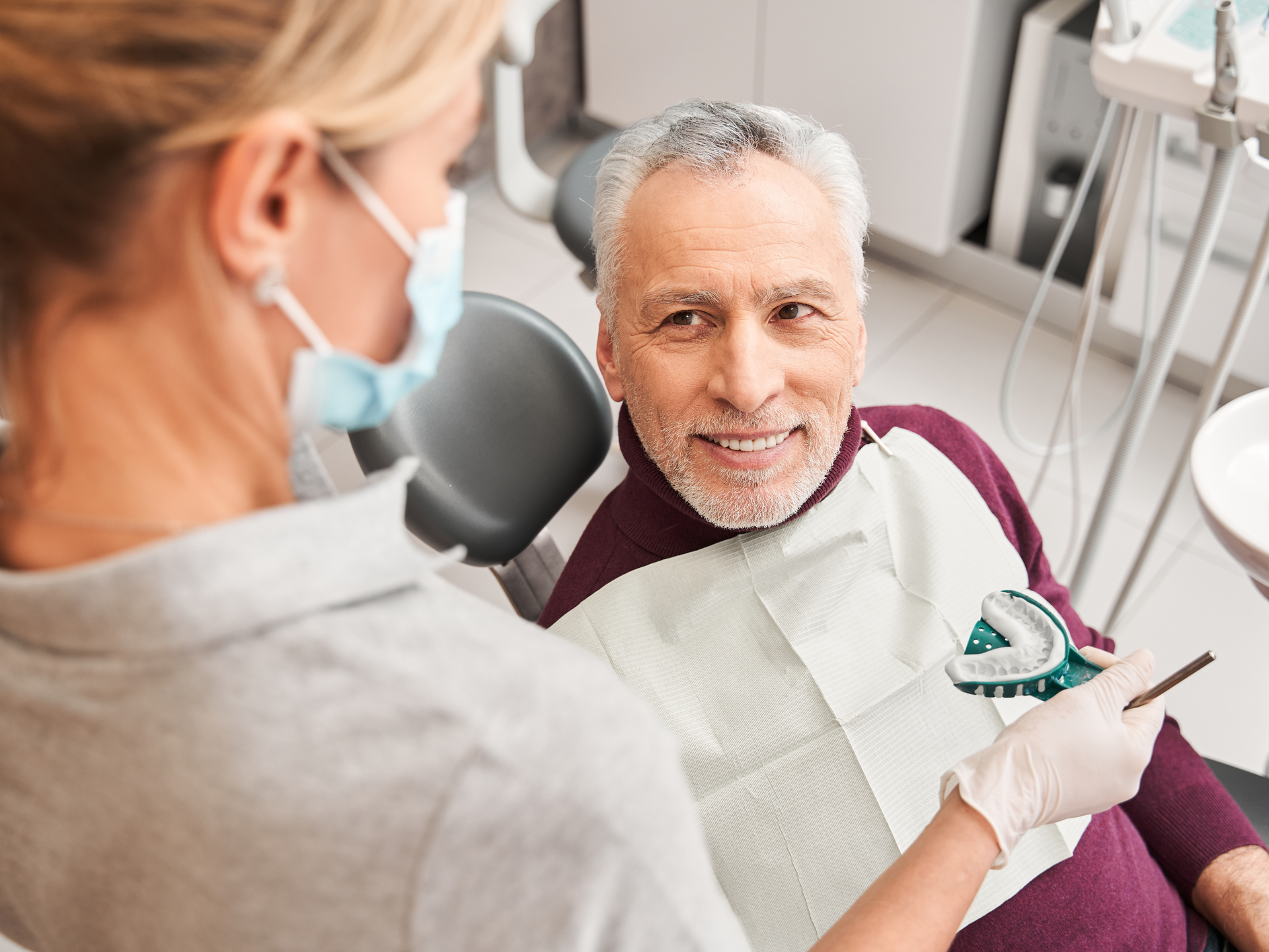 A man is sitting in a dental chair while a dentist examines his teeth .
