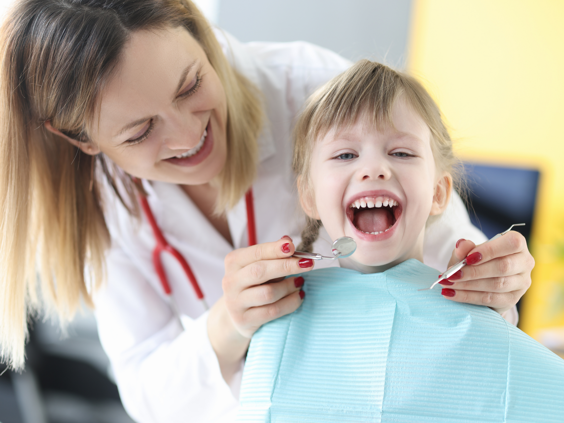 a female dentist is examining a little girl 's teeth in a dental office .