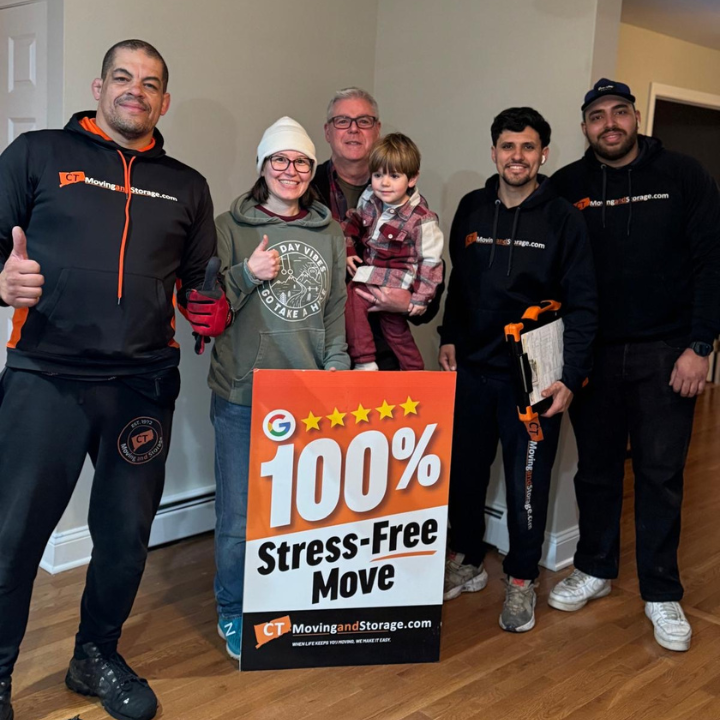 Group of movers and a family smile next to a sign for a