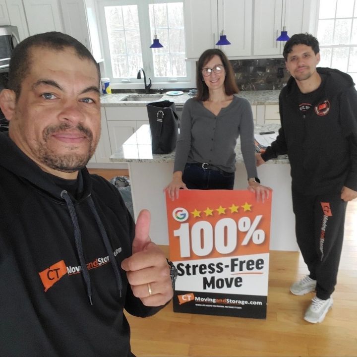 Three people in a bright kitchen holding a “100% Stress-Free Move” sign, one giving a thumbs-up