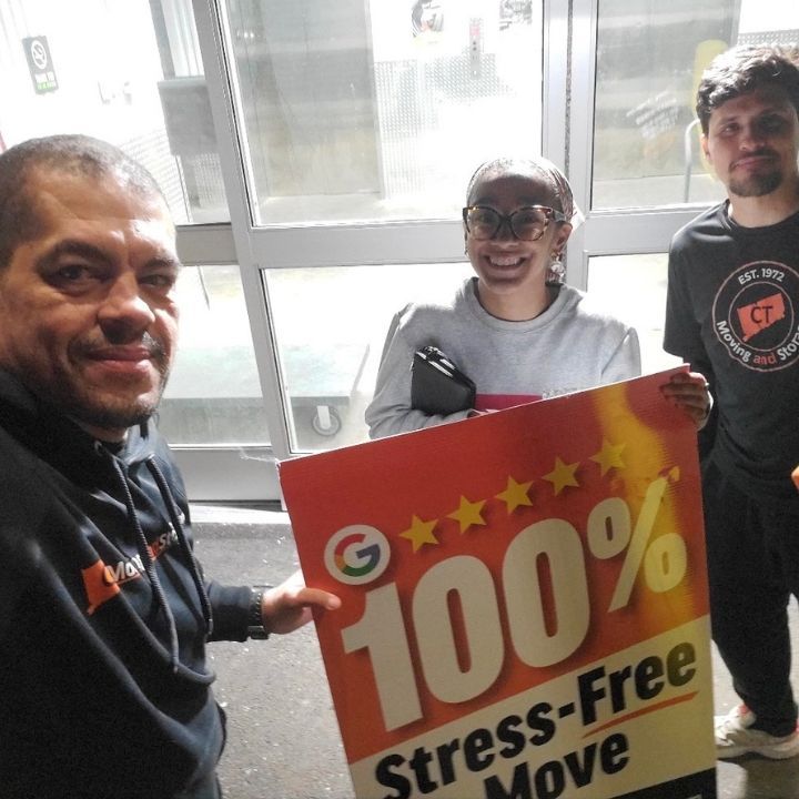 Three people indoors holding a bright red “100% Stress-Free Move” sign