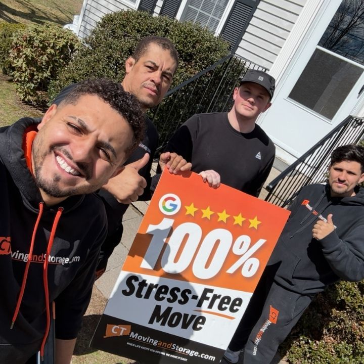 Four movers posing outdoors holding a sign that says “100% Stress-Free Move”