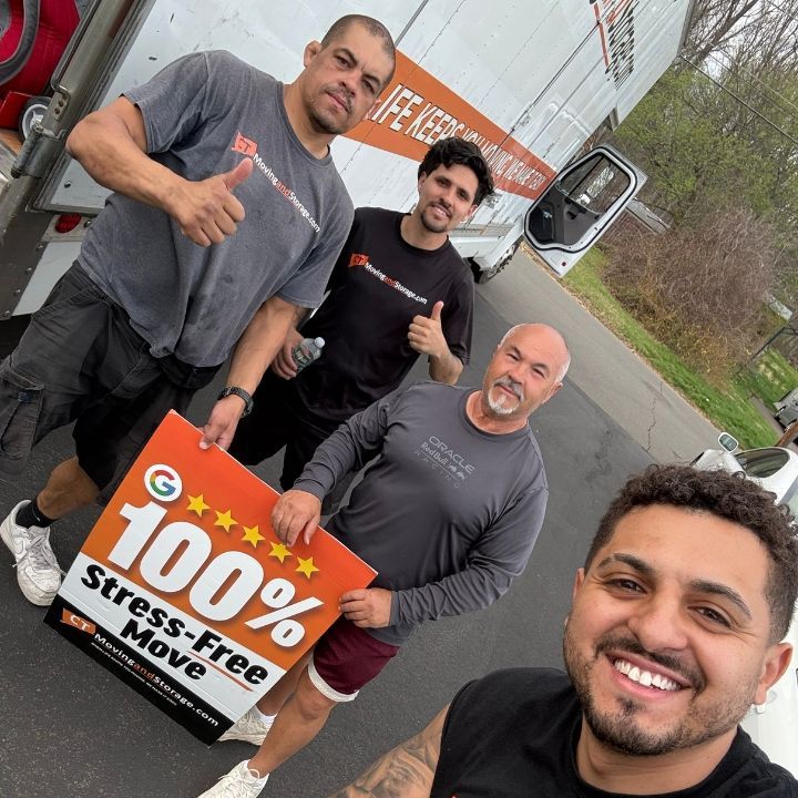 Four smiling movers posing by a truck, holding a “100% Stress-Free Move” sign.