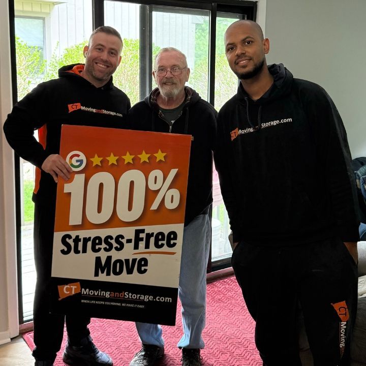 Three men hold a “100% Stress-Free Move” sign in a bright office.