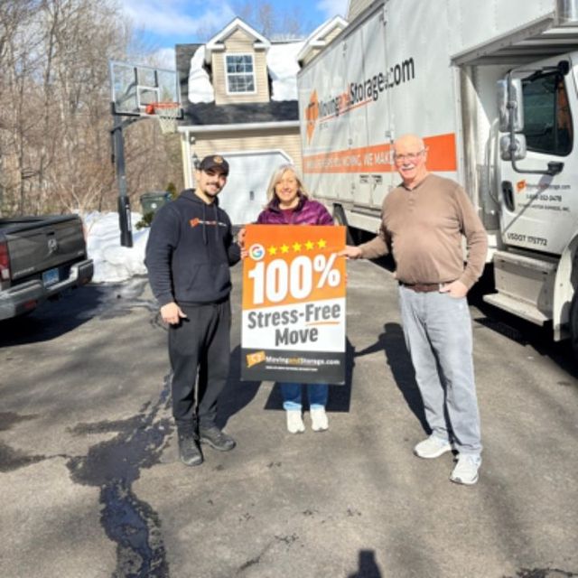 Movers with smiling customers beside moving truck, holding sign 