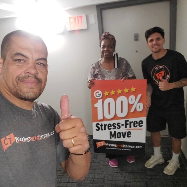 Three people in a hallway hold a “100% Stress-Free Move” sign; one gives a thumbs up.