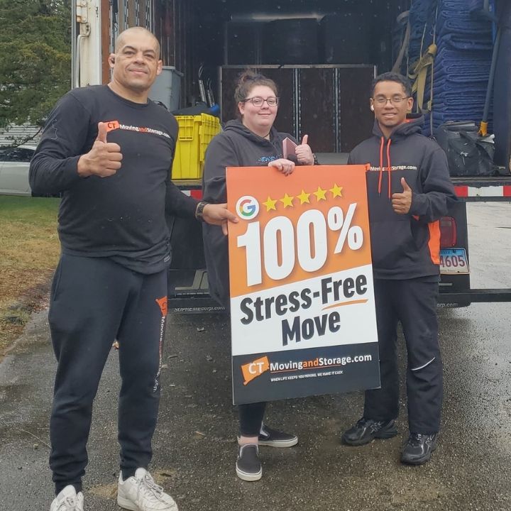 Three movers holding a “100% Stress Free Move” sign in front of a moving truck.