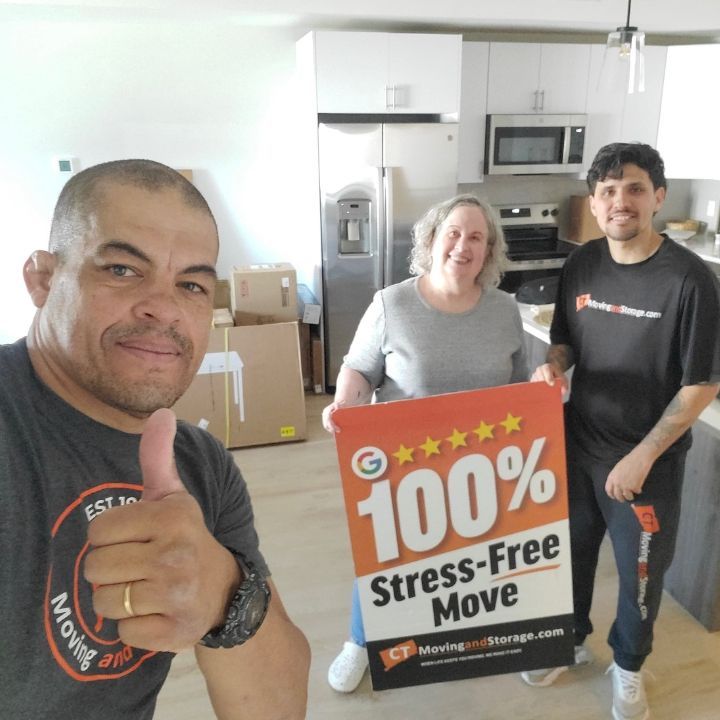 Three people holding a “100% Stress-Free Move” sign in a bright kitchen.