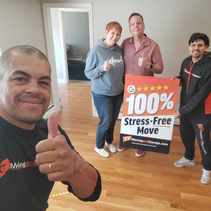 Three people in a new home holding a “100% Stress-Free Move” sign and smiling.