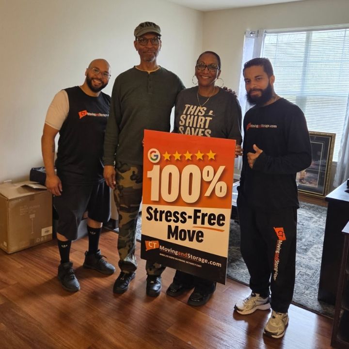 Four people indoors holding a sign that reads “100% Stress-Free Move”