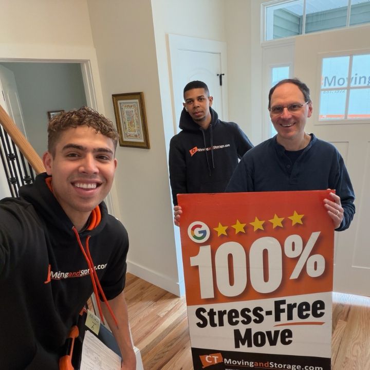 Three men holding a red “100% Stress-Free Move” sign in a bright hallway