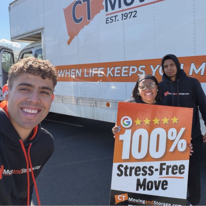 Three people posing by a CT Moving truck holding a “100% Stress-Free Move” sign