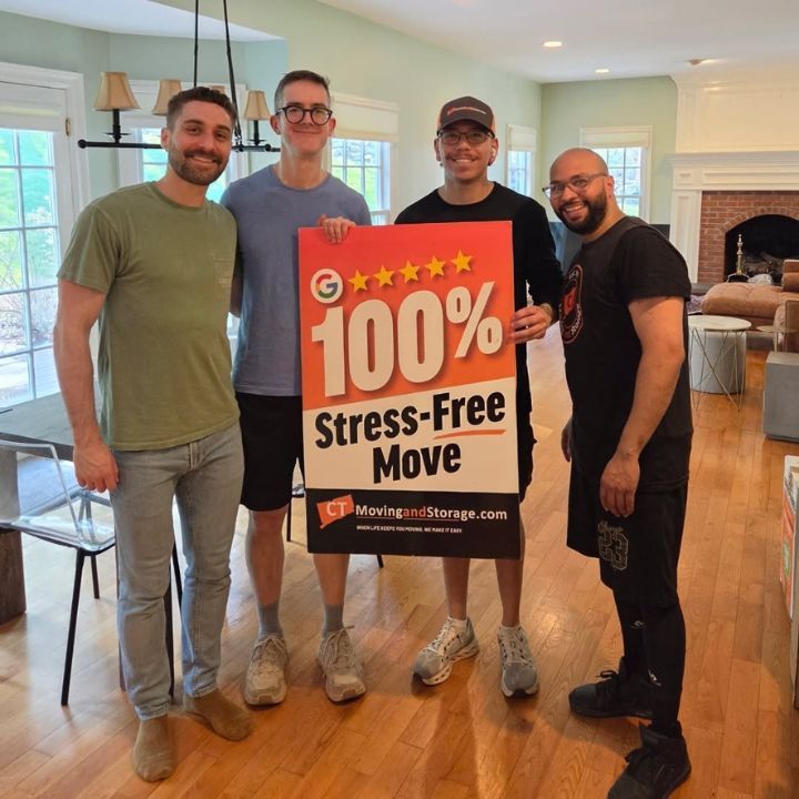 Four people indoors holding a “100% Stress-Free Move” sign at a moving company office