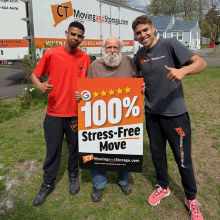 Three men holding a “100% Stress-Free Move” sign beside a moving truck outdoors.