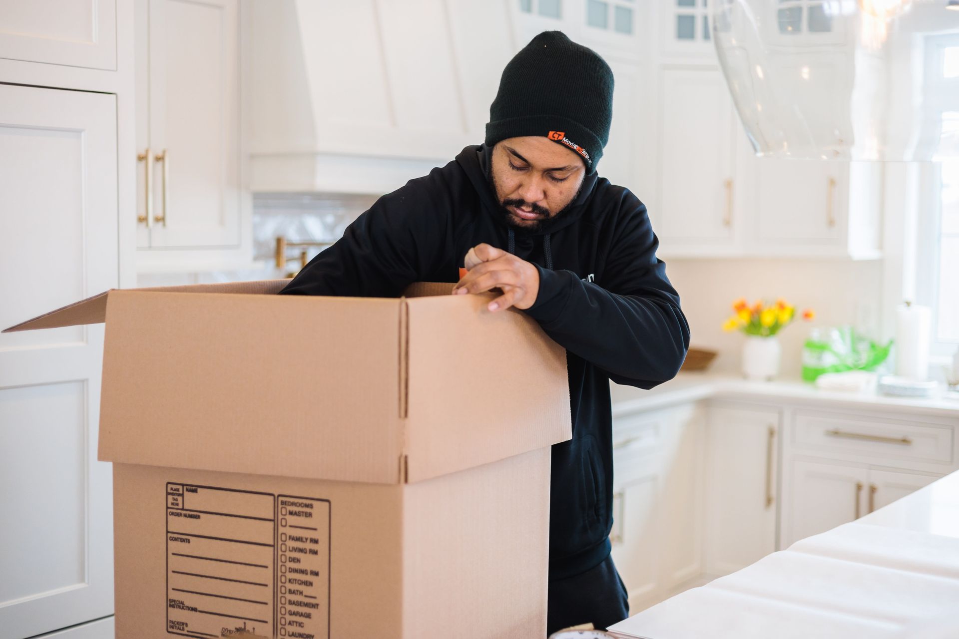 Man opening a cardboard box in a kitchen with white cabinets.