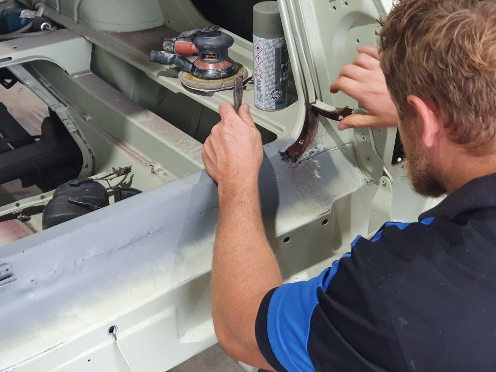 A Man Is Working On A Car In A Garage — East Coast Panel & Paint In Woolgoolga, NSW