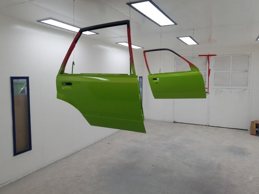 A Green Car Door Is Hanging From The Ceiling In A Paint Booth — East Coast Panel & Paint In Woolgoolga, NSW