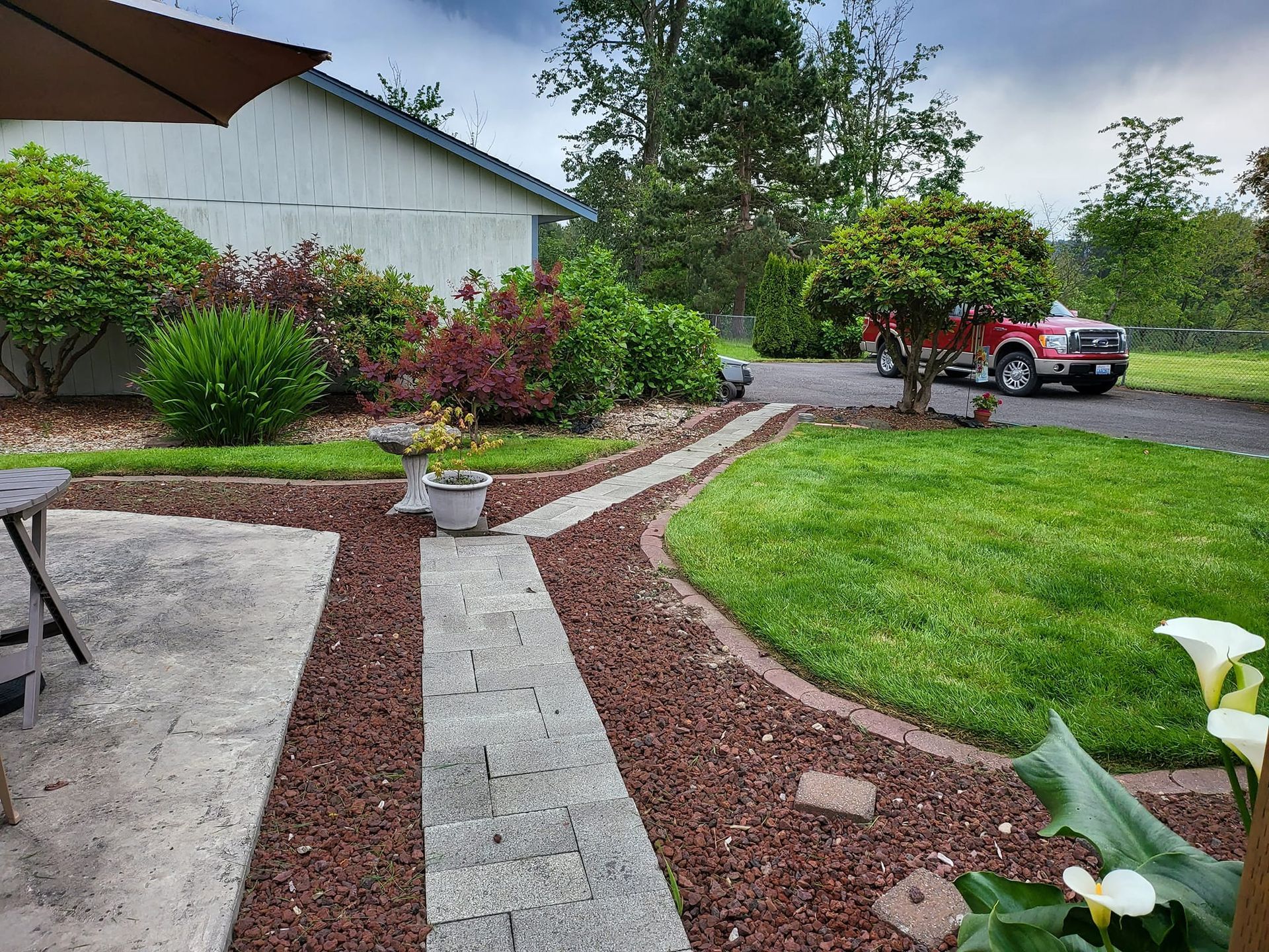 Lush landscaped yard with red truck parked on driveway. Walkway leads to the house, surrounded by red rock.