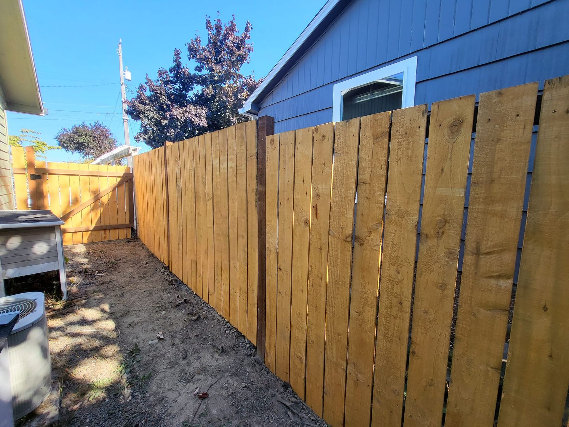 Wooden fence in a yard against a blue house and sunny sky.