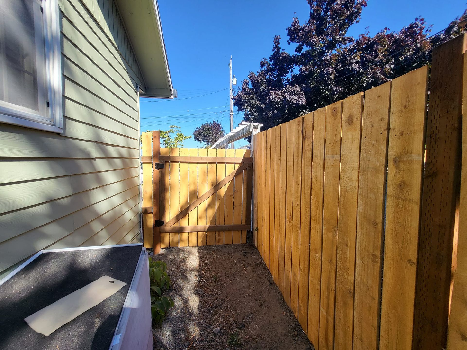 Wooden fence and gate next to a house with light green siding and a gravel pathway.