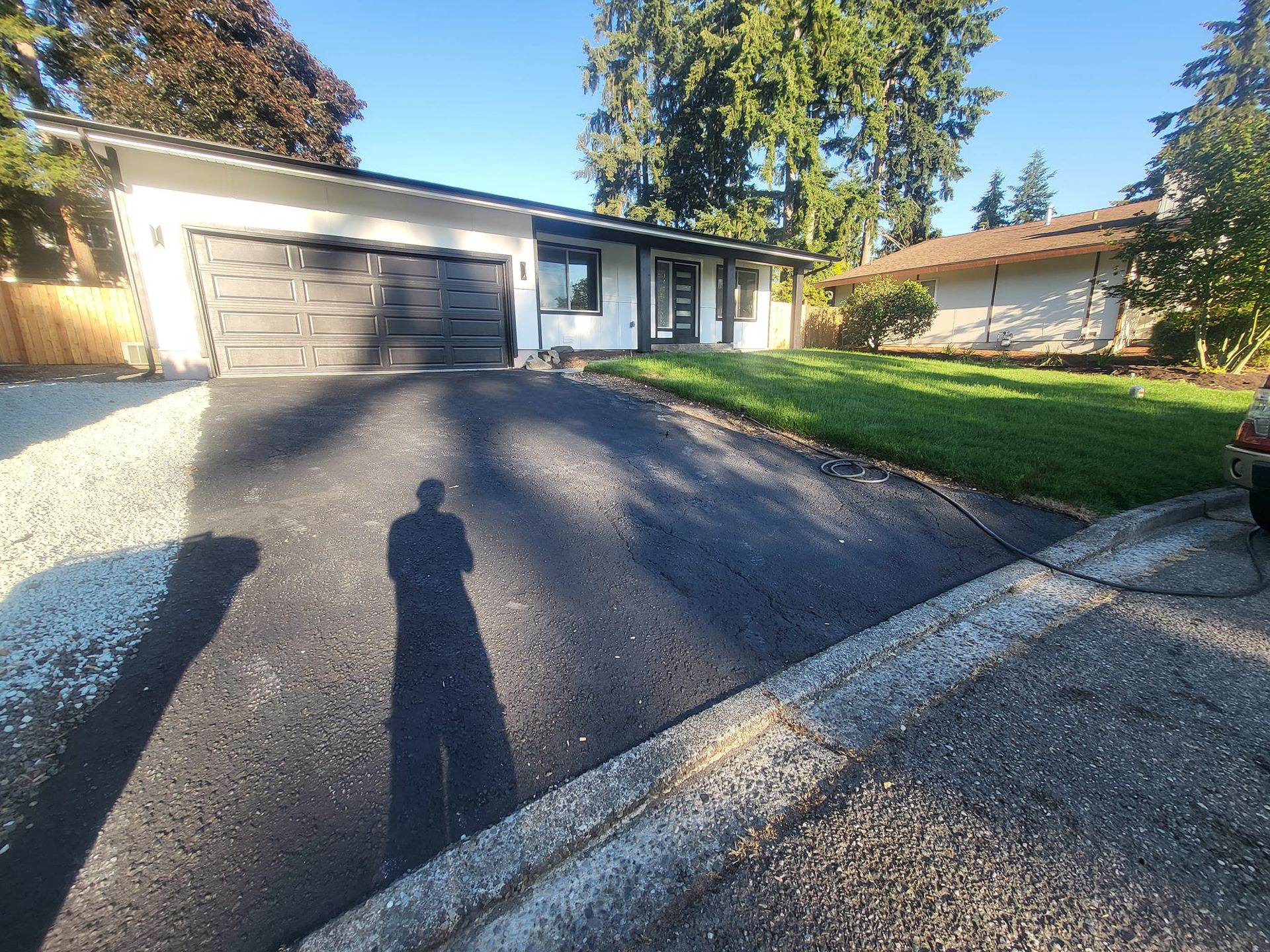 House with a newly paved asphalt driveway, green lawn, and person's shadow.