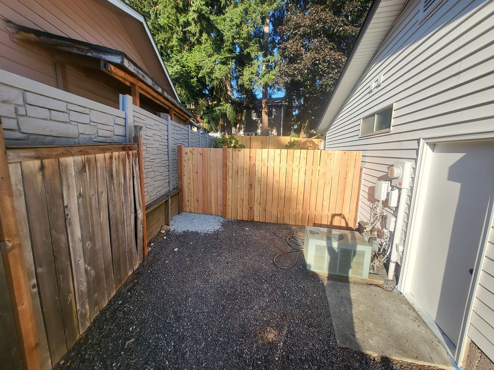 A narrow backyard with gravel, flanked by wooden fences and a garage.