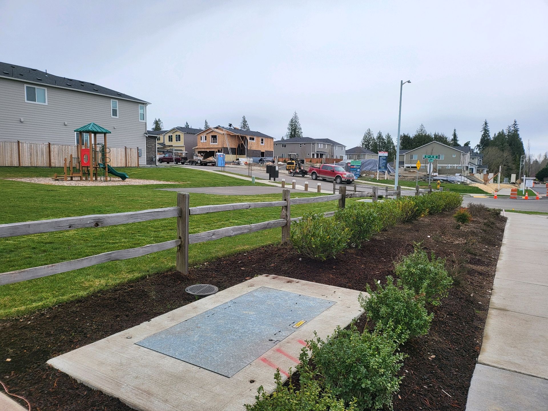 Park with playground and fence, residential neighborhood in the background, cloudy day.