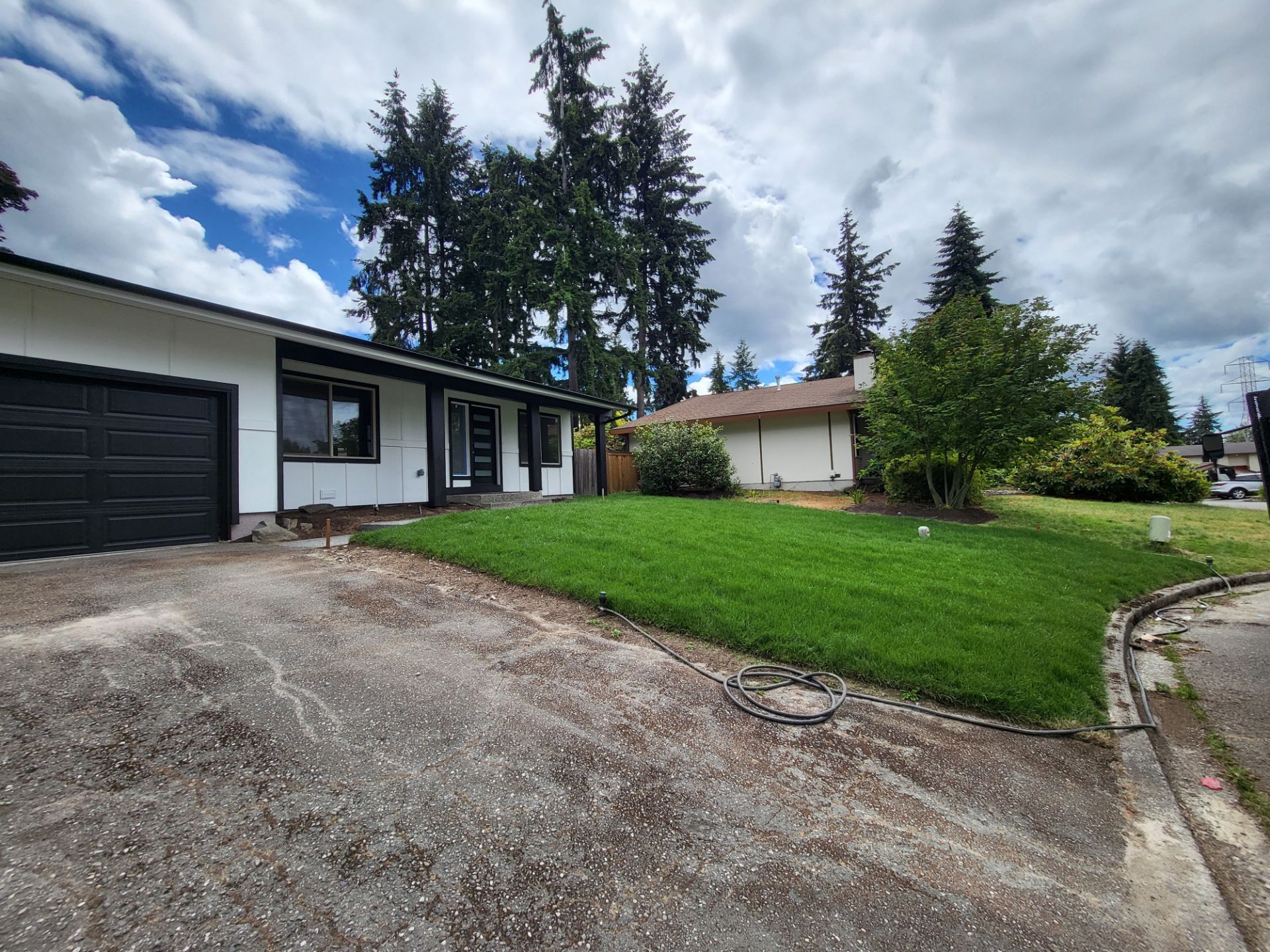 Front view of a house with a black garage door, white walls, and a green lawn under a cloudy sky.