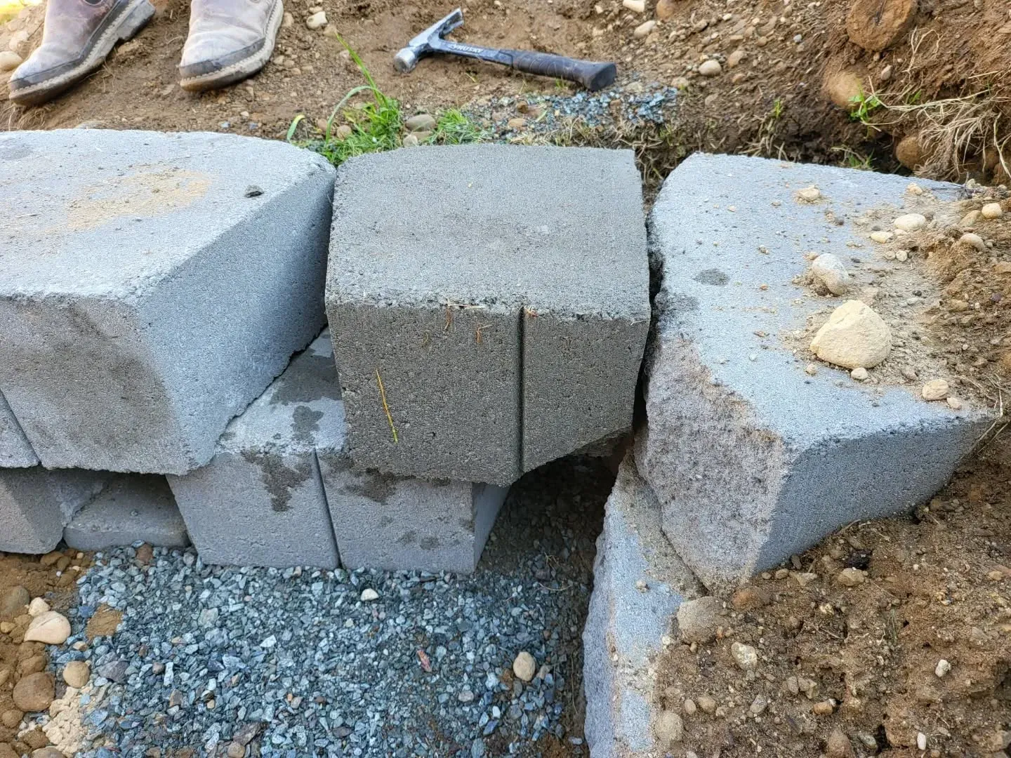 Construction of a retaining wall with gray concrete blocks, hammer nearby.