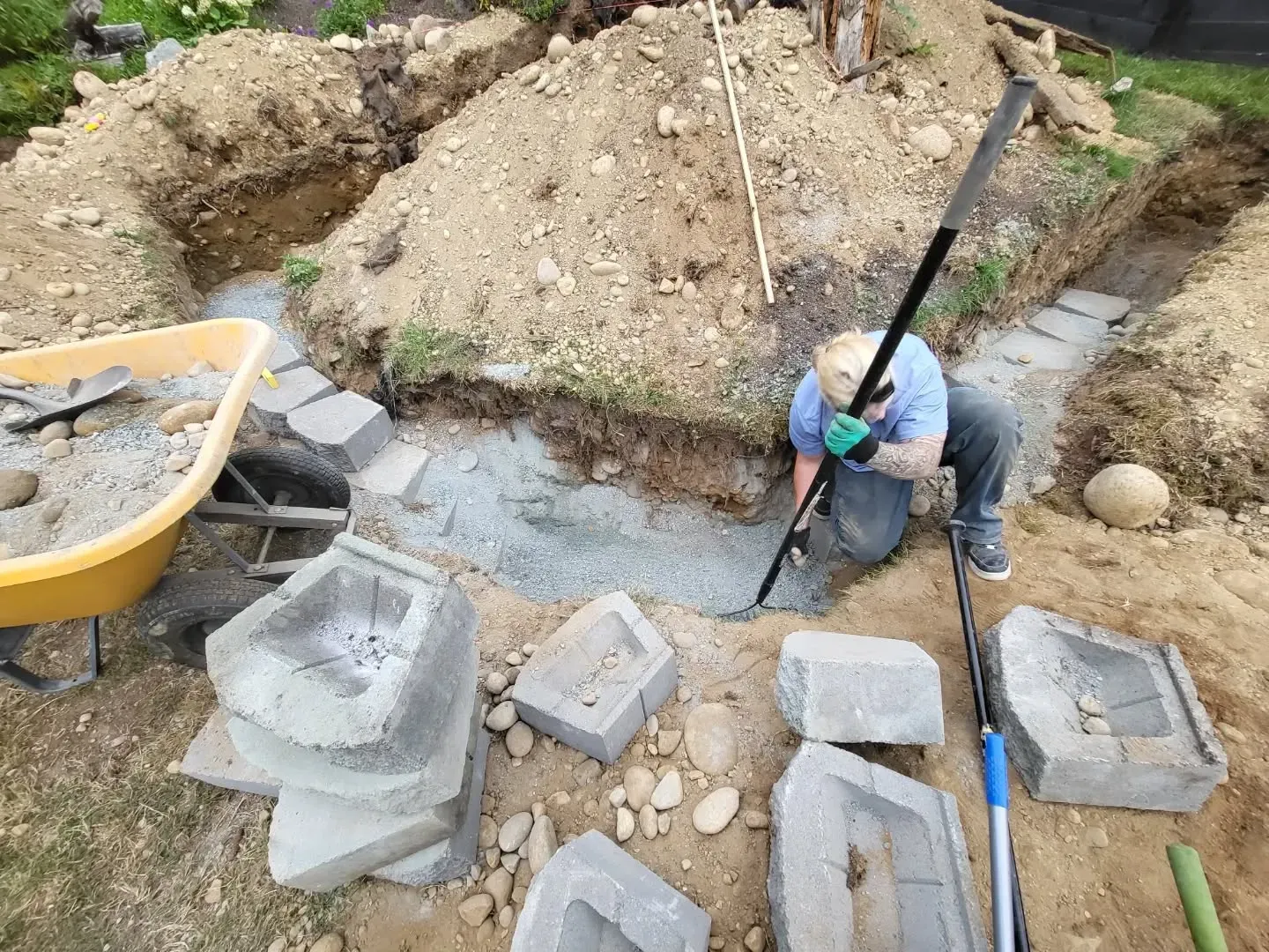 Person using a tool to work on a path construction project, surrounded by blocks and dirt.