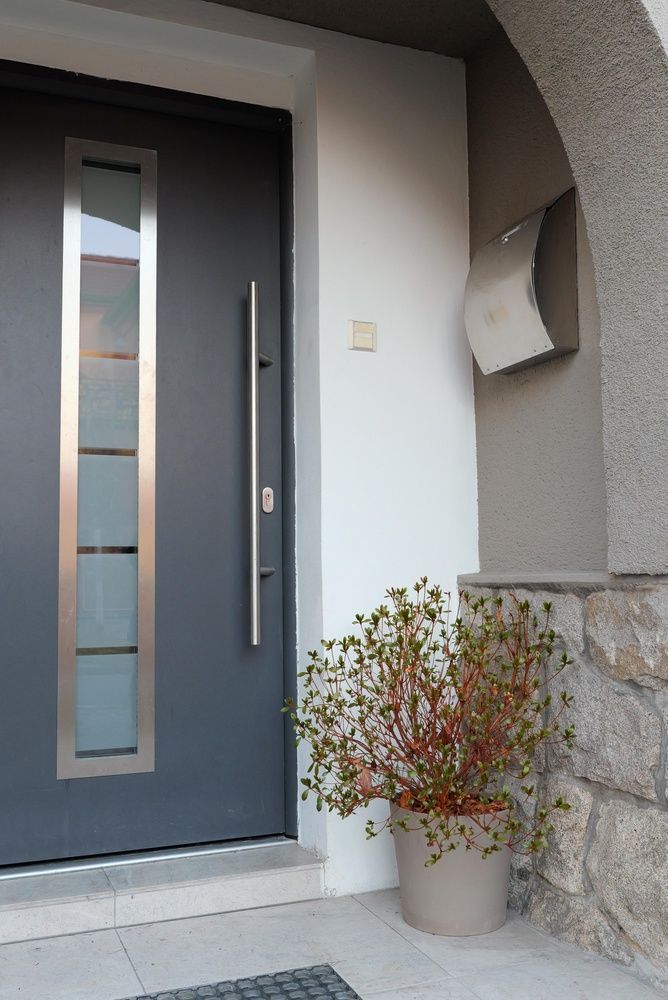 Gray front door with vertical glass panels, a long silver handle, and a potted plant.