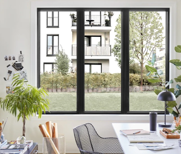 Interior office view through a large window. A desk, chair, and plants are visible.