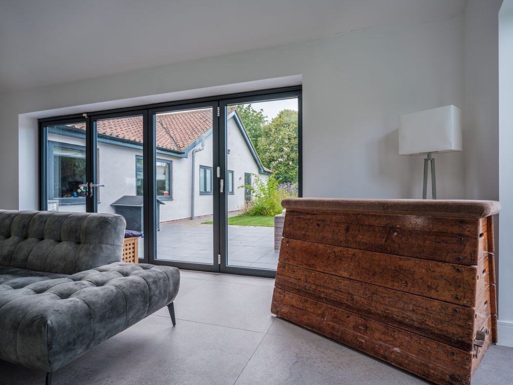 Interior view: gray couch, wooden cabinet, and glass doors leading to a backyard with a white house.
