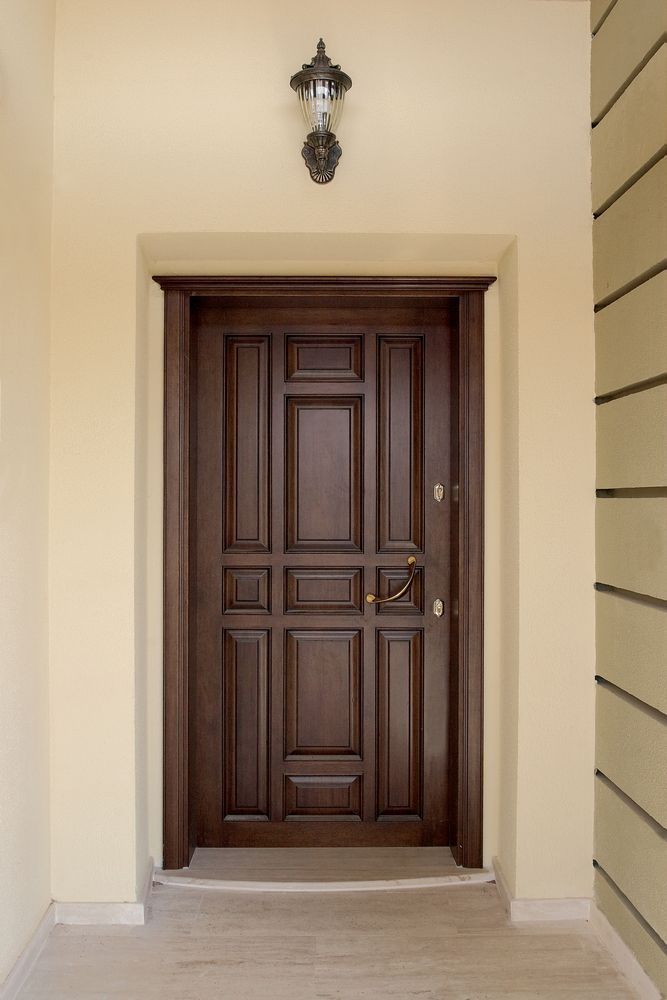 Brown wooden front door with panel design, under a small lamp.