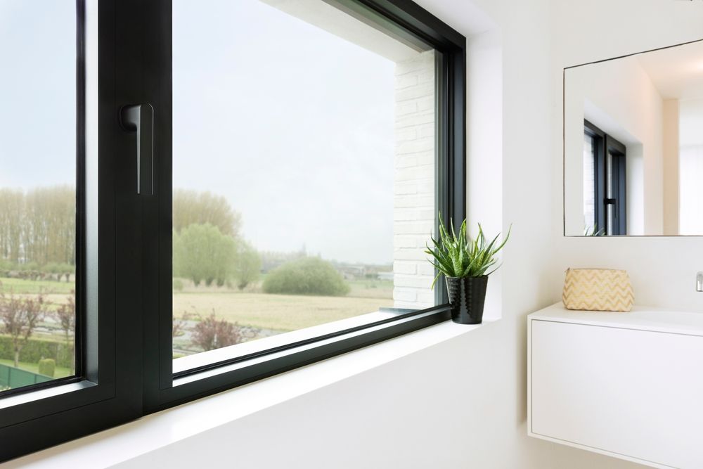 Interior office view through a large window. A desk, chair, and plants are visible.