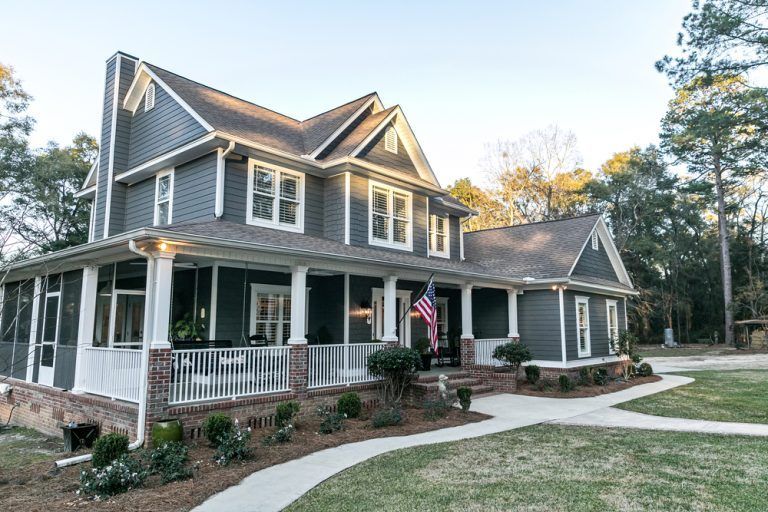 A large gray house with a large porch and a walkway leading to it.