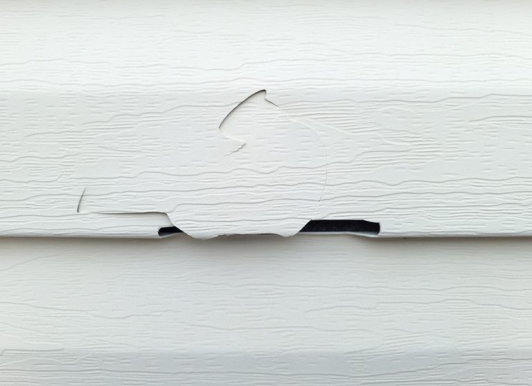 A close up of a white siding with a hole in it.