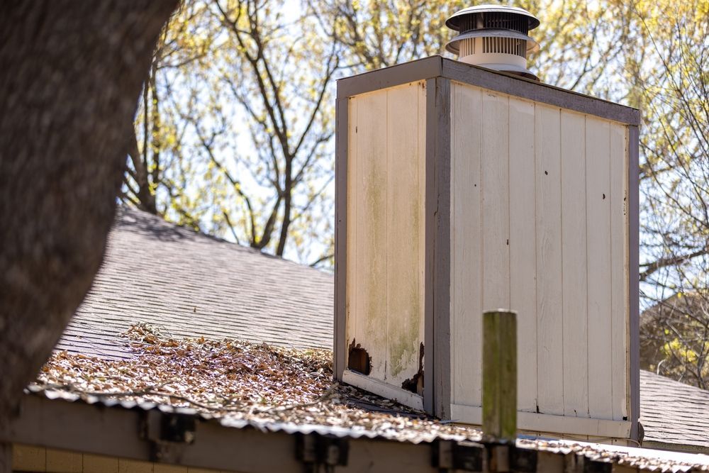 A chimney is sitting on top of a roof next to a tree.