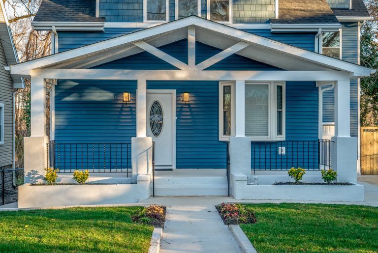 A blue house with a white porch and a walkway leading to it.