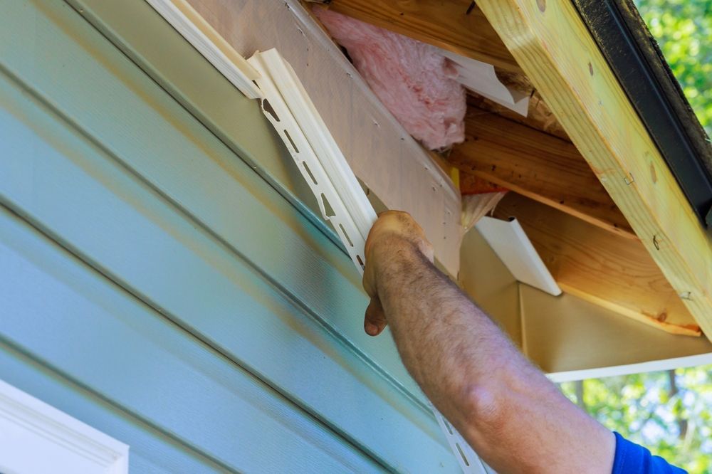 A man is installing siding on the side of a house.