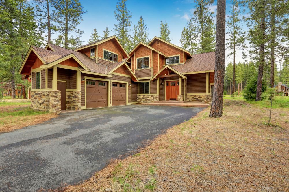 A large house in the middle of a forest with a driveway leading to it.