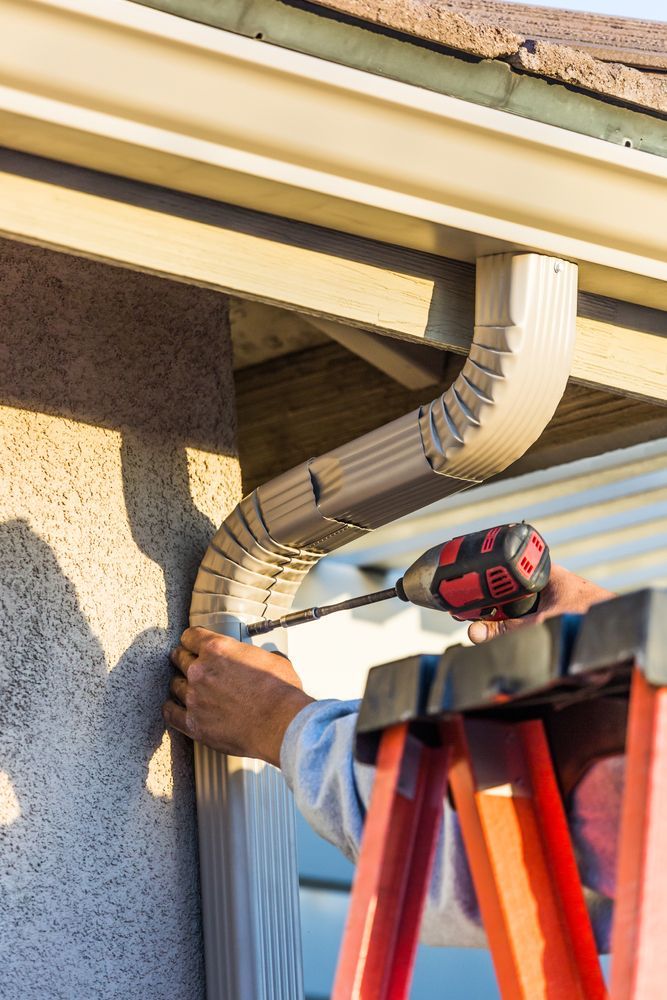 A man is using a drill to install a gutter on a house.