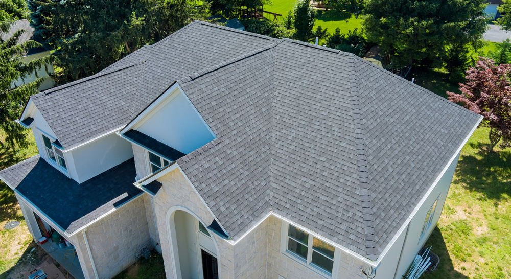 An aerial view of a two-story residential house with light-colored brick, white trim, and a dark gray shingle roof.