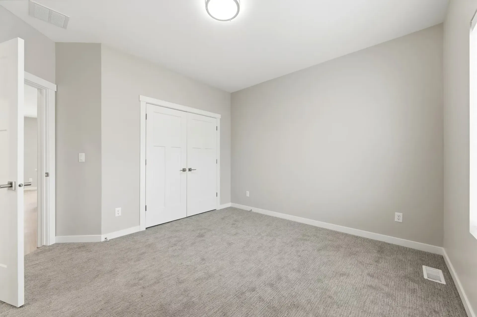 Empty bedroom with gray walls, white trim, carpet, and double closet doors.